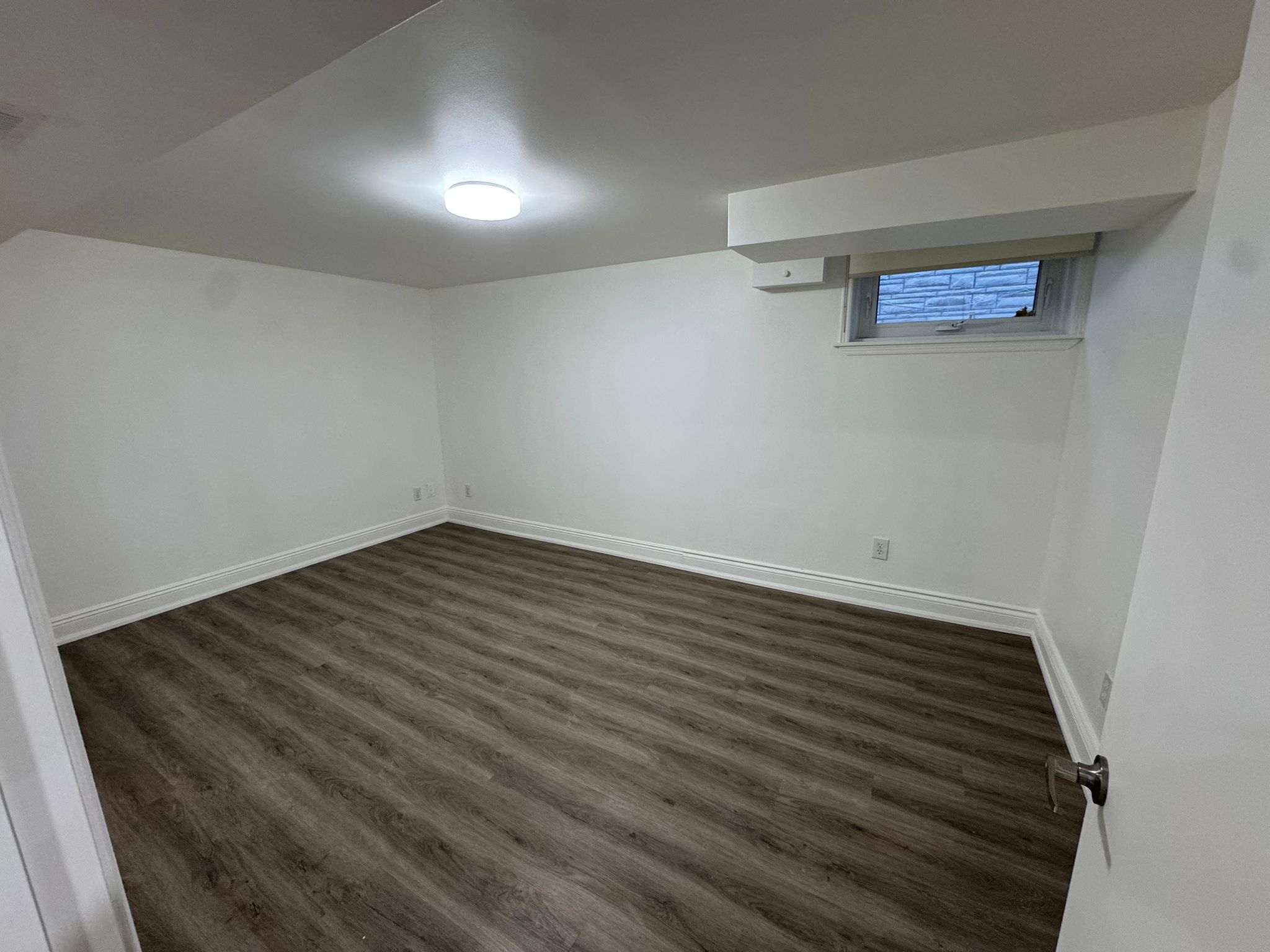 Basement bedroom with dark vinyl plank flooring and egress window